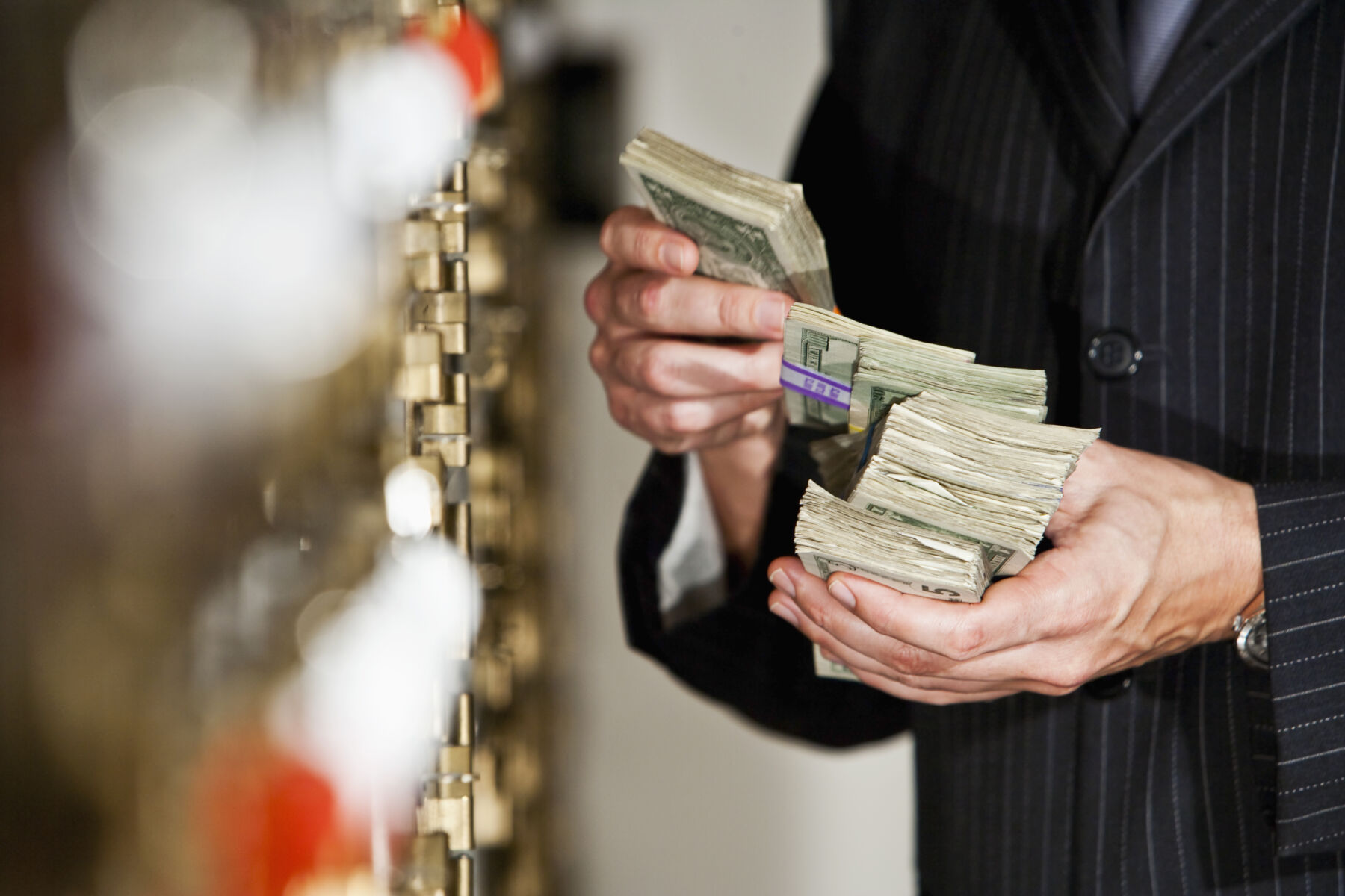 Man holding big stack of US paper currency by safety deposit boxes.  Focus on money